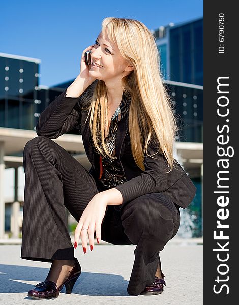 Happy young blond business woman squats and talking on a phone. Happy young blond business woman squats and talking on a phone