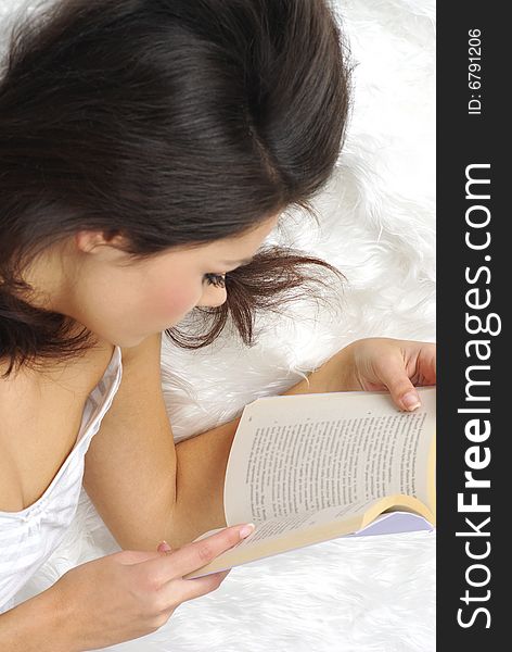 Beautiful young woman reading book in bed