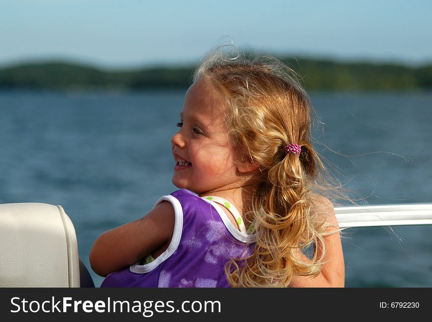 A three year-old girl – wearing her lifejacket – smiles back at one of her parents while riding on a boat out on a lake on a sunny afternoon. A three year-old girl – wearing her lifejacket – smiles back at one of her parents while riding on a boat out on a lake on a sunny afternoon.