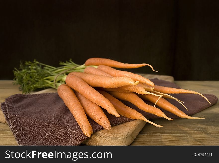 A bunch of fresh carrots on a brown napkin on a wooden surface. 
Space for text on top.