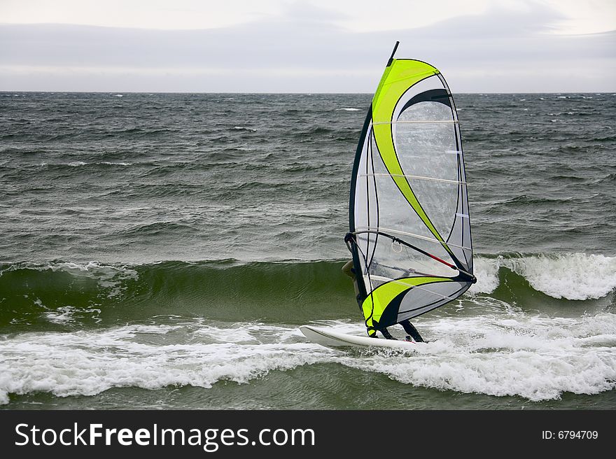 Windsurfer gliding on waves in overcast day. Windsurfer gliding on waves in overcast day