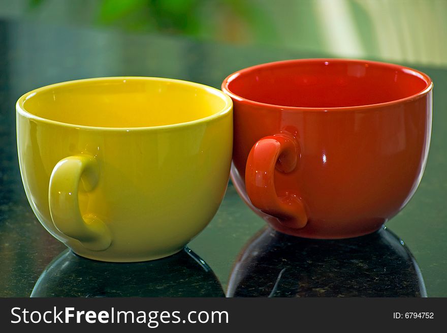 A yellow and orange coffee mug sit on a marble countertop. A yellow and orange coffee mug sit on a marble countertop