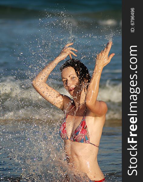 A young woman splashes in the shallows at the beach. A young woman splashes in the shallows at the beach