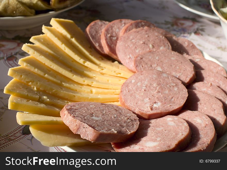 Sausage and cheese are cut on a plate. Sausage and cheese are cut on a plate