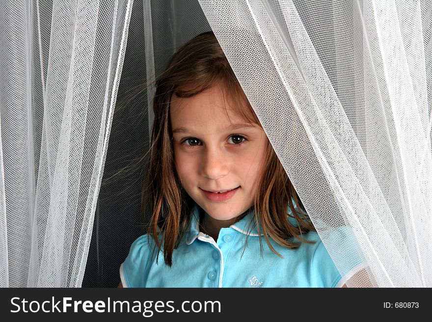 Young girl looking out from behind netting or curtains. Young girl looking out from behind netting or curtains