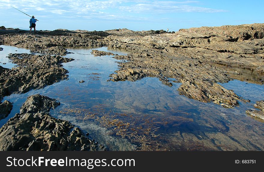 Rocky outcrop by the sea with man heading out with his fishing pole over his shoulder. Rocky outcrop by the sea with man heading out with his fishing pole over his shoulder