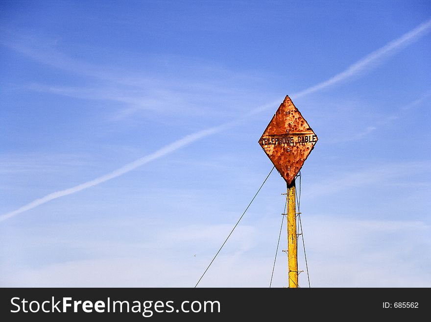 A diamond shaped rusted telephone cable sign post against a blue sky. A diamond shaped rusted telephone cable sign post against a blue sky.
