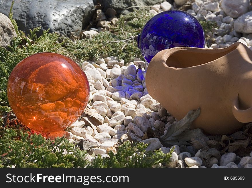 Orange and blue glass balls in a garden rockery with a terracotta pot,. Orange and blue glass balls in a garden rockery with a terracotta pot,