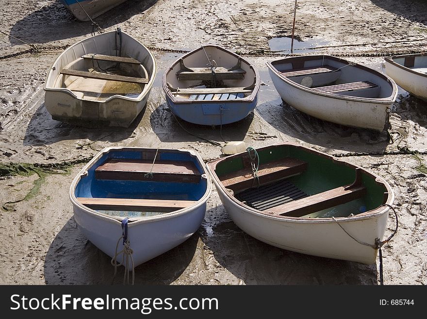 A group of small rowing boats anchored in a bay at low tide.