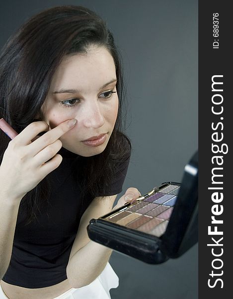 Attractive young woman holding some make-up and checking up her face in the mirror. Attractive young woman holding some make-up and checking up her face in the mirror