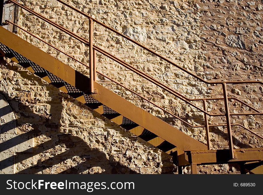 A stone wall acts as a backdrop to a metal staircase. A stone wall acts as a backdrop to a metal staircase.
