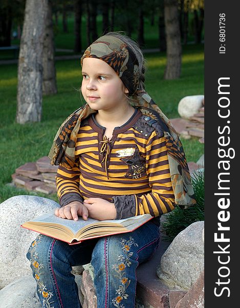 Little girl sitting and reading a book in the park. Little girl sitting and reading a book in the park