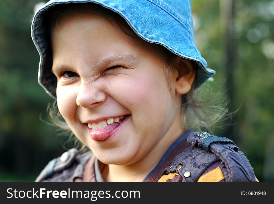 Funny little girl in blue hat showing tongue