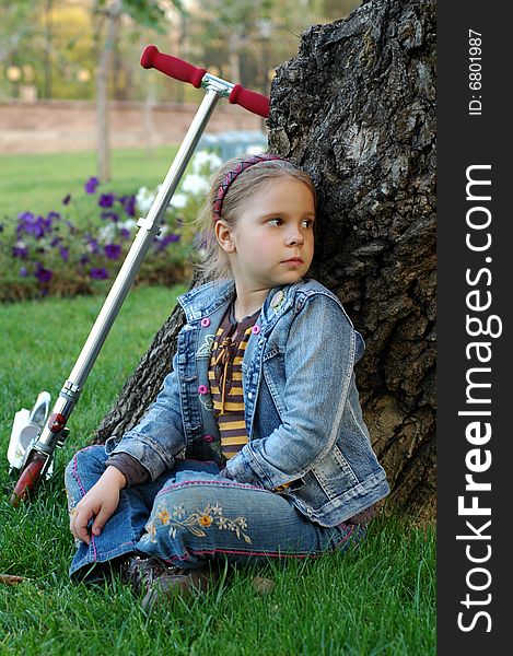 Little girl with scooter sitting under the tree