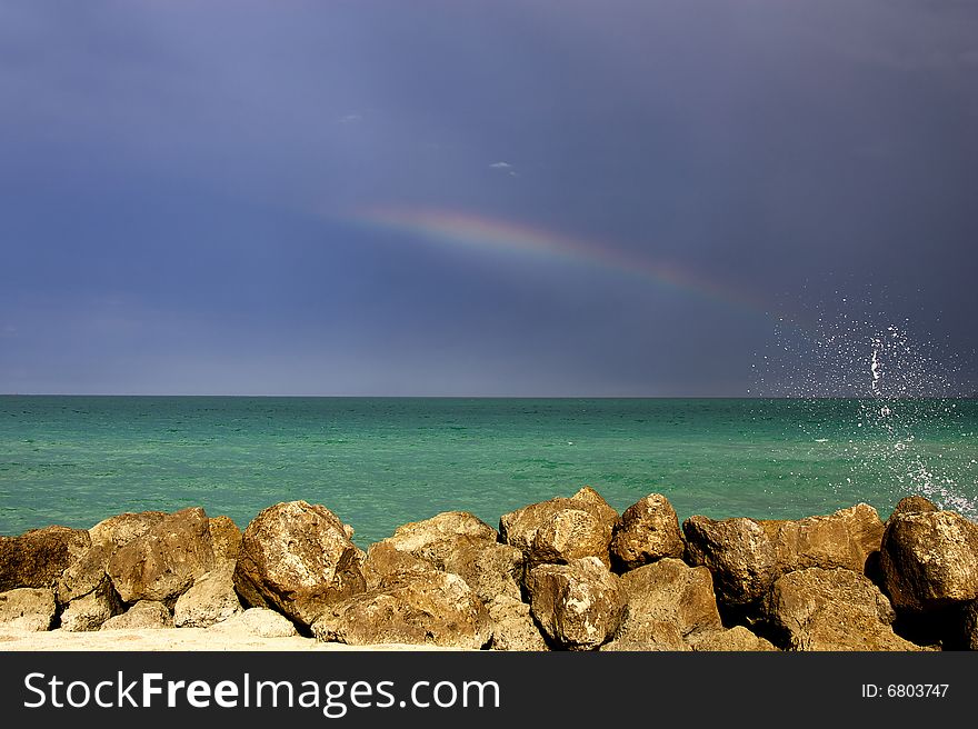 Little rainbow above ocean, blue sky and clounds