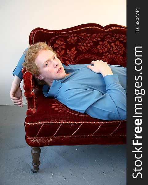 A young red-haired man lying on an old red sofa. A young red-haired man lying on an old red sofa.