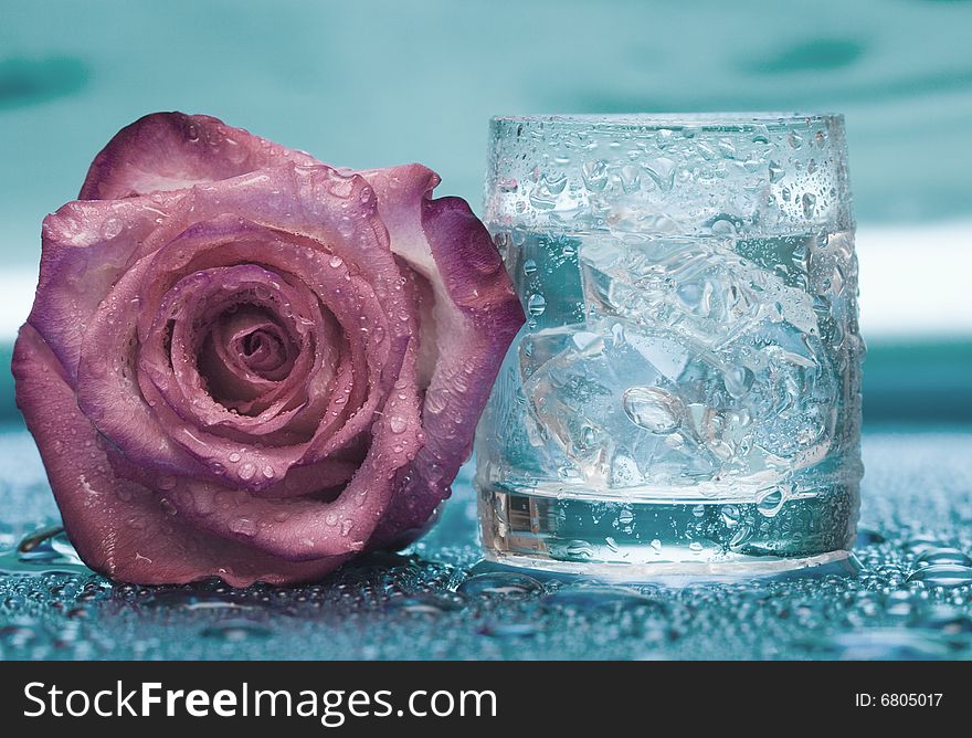 Glass with water and rose over blue