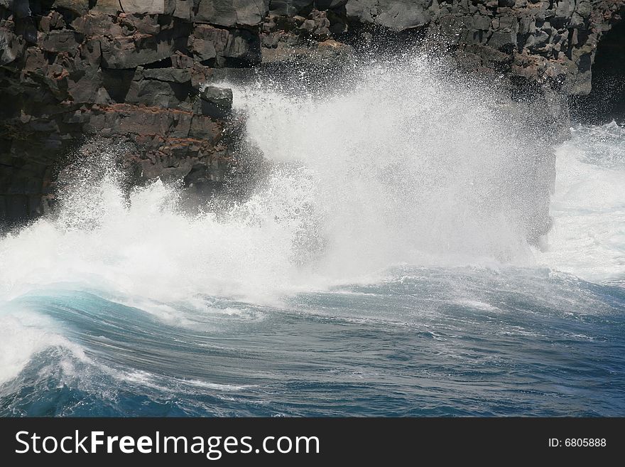 A hard blue wave crashes against a cliff on the coast. A hard blue wave crashes against a cliff on the coast