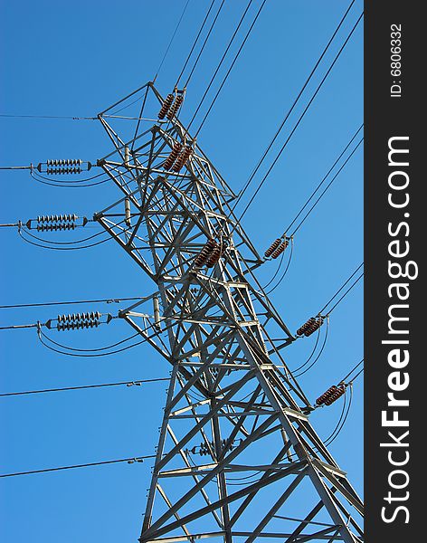 High voltage electric transmission tower or electricity pylon viewed from a low angle and set against a bright, clear blue sky. High voltage electric transmission tower or electricity pylon viewed from a low angle and set against a bright, clear blue sky