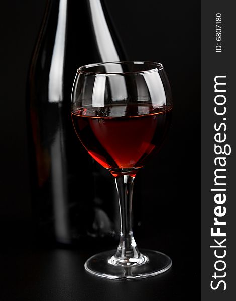 Glass of red wine and bottle over black background