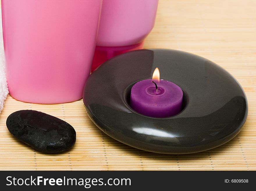 Pink bottle of shampoo with candle and pebble