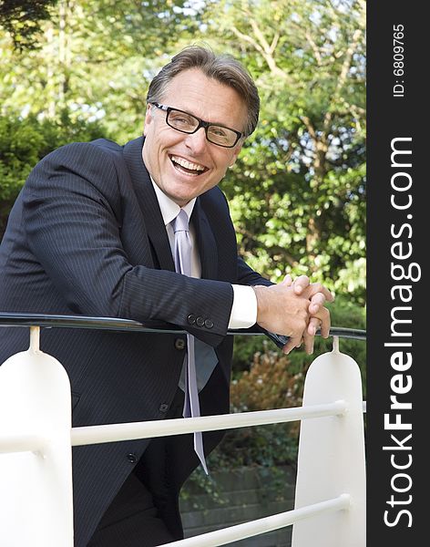 Handsome forties businessman wearing spectacles is leaning on railings and laughing. Handsome forties businessman wearing spectacles is leaning on railings and laughing