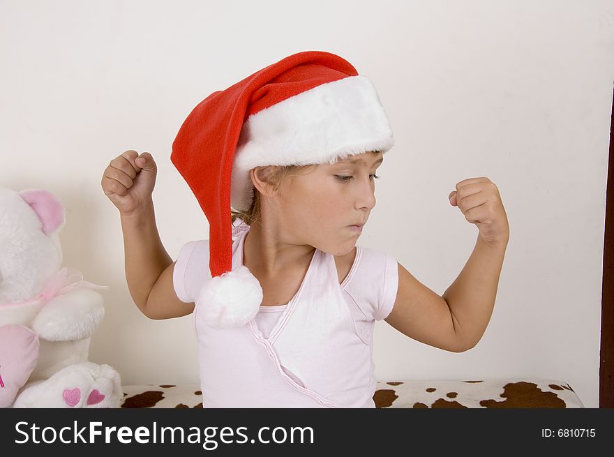 Little girl wearing christmas hat and showing her muscles