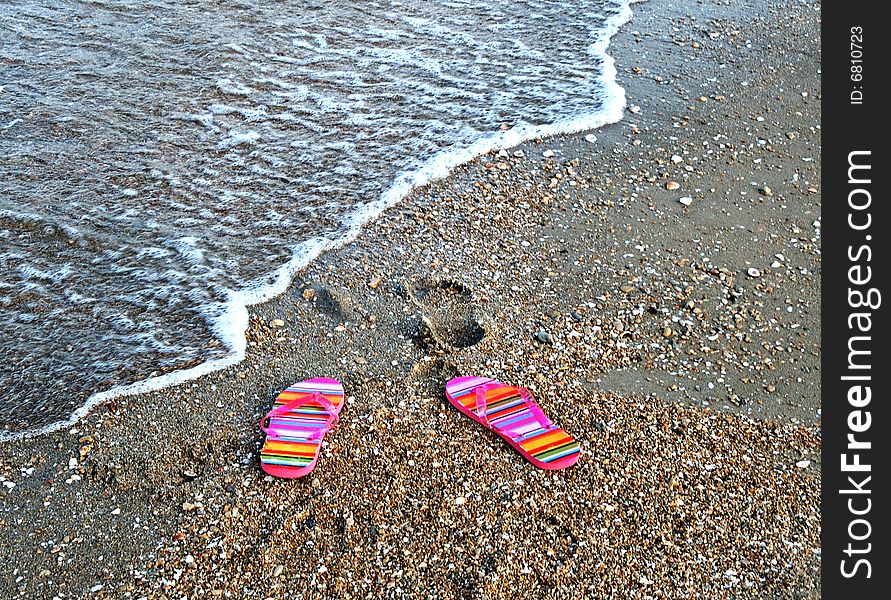 A pair of colorful flip-flop sandals on a sea beach. A pair of colorful flip-flop sandals on a sea beach