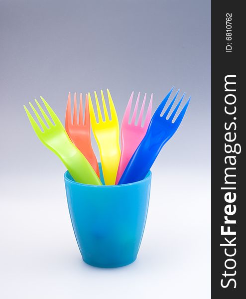 Rainbow-coloured plastic picnic forks in a plastic cup. Continuous background with copy space. Rainbow-coloured plastic picnic forks in a plastic cup. Continuous background with copy space.