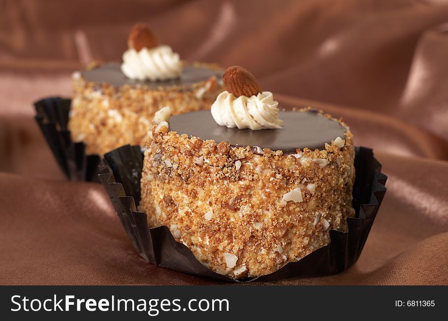 Two miniature chocolate meringue cakes with cream and almonds on golden silk background. Two miniature chocolate meringue cakes with cream and almonds on golden silk background