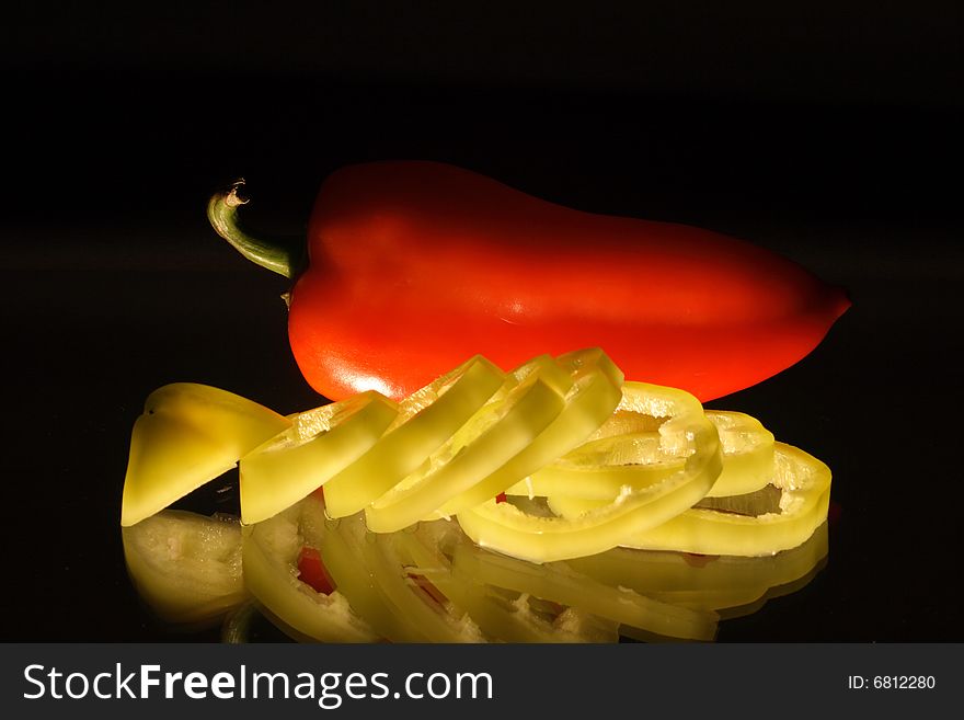 Red and slit green pepper with reverberation lying on black background. Red and slit green pepper with reverberation lying on black background