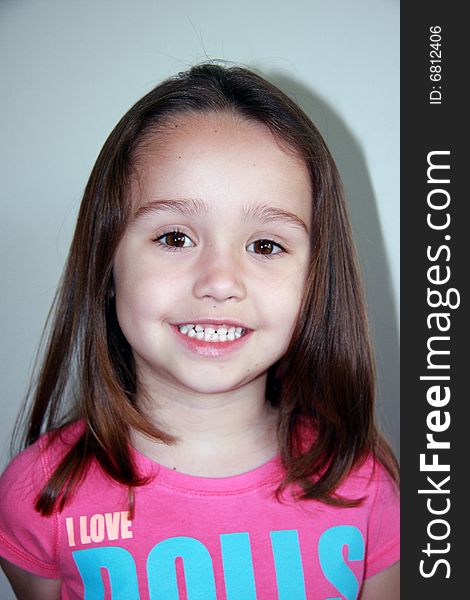 Portrait of a smiling 4 year old caucasion female child, with shoulder length straight brown hair, and a pink collarless tshirt displaying the motiff -'I love dolls'. Portrait of a smiling 4 year old caucasion female child, with shoulder length straight brown hair, and a pink collarless tshirt displaying the motiff -'I love dolls'.