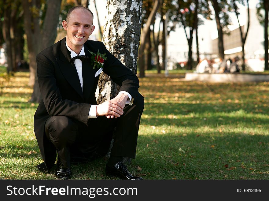 Smiling groom sitting near a birch. Smiling groom sitting near a birch