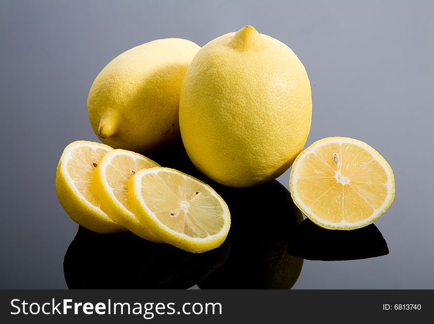 Sliced and whole yellow lemons on mirrored background. Sliced and whole yellow lemons on mirrored background