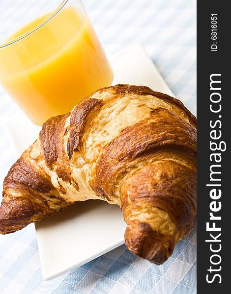 Fresh croissant with orange juice on a blue cloth