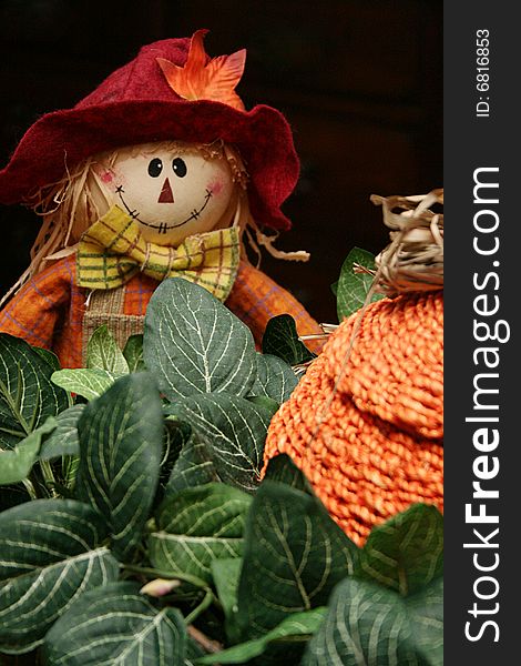 A toy scarecrow sits with a straw pumpkin and some ivy.