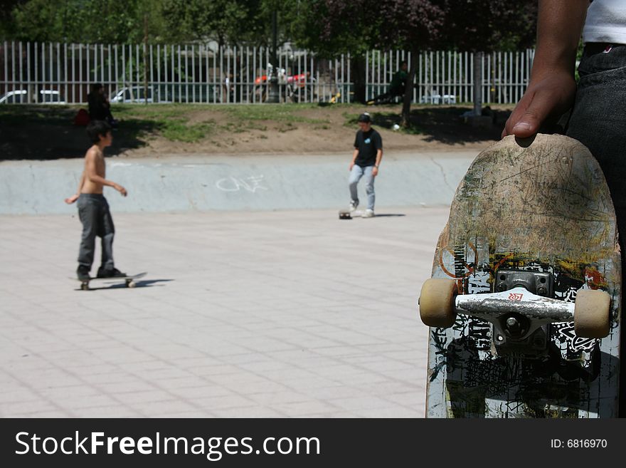 A kid showing his skate board with another skaters on the background