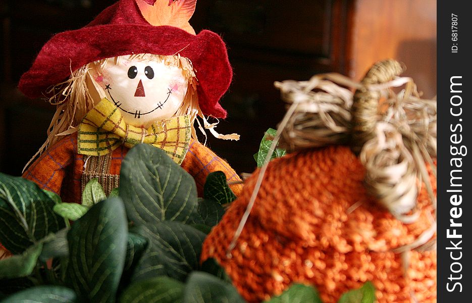 A toy scarecrow sits with a straw pumpkin and some ivy. A toy scarecrow sits with a straw pumpkin and some ivy.