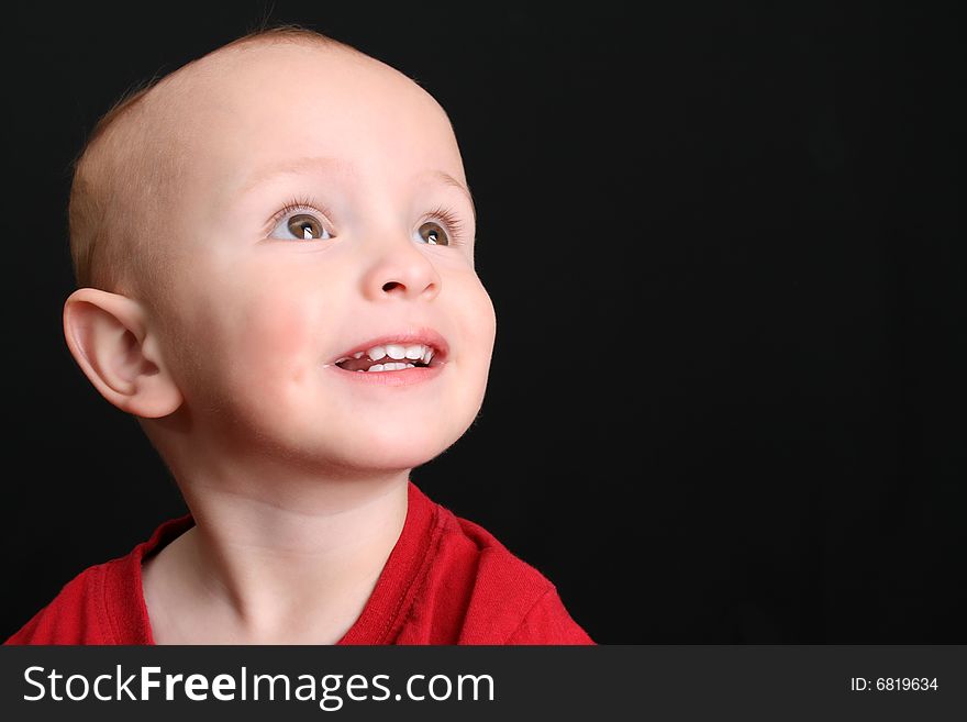 Blonde toddler against a black background looking up