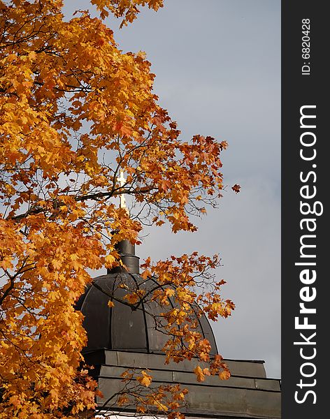 Dome of chapel with a gold cross and tree with an autumn foliage