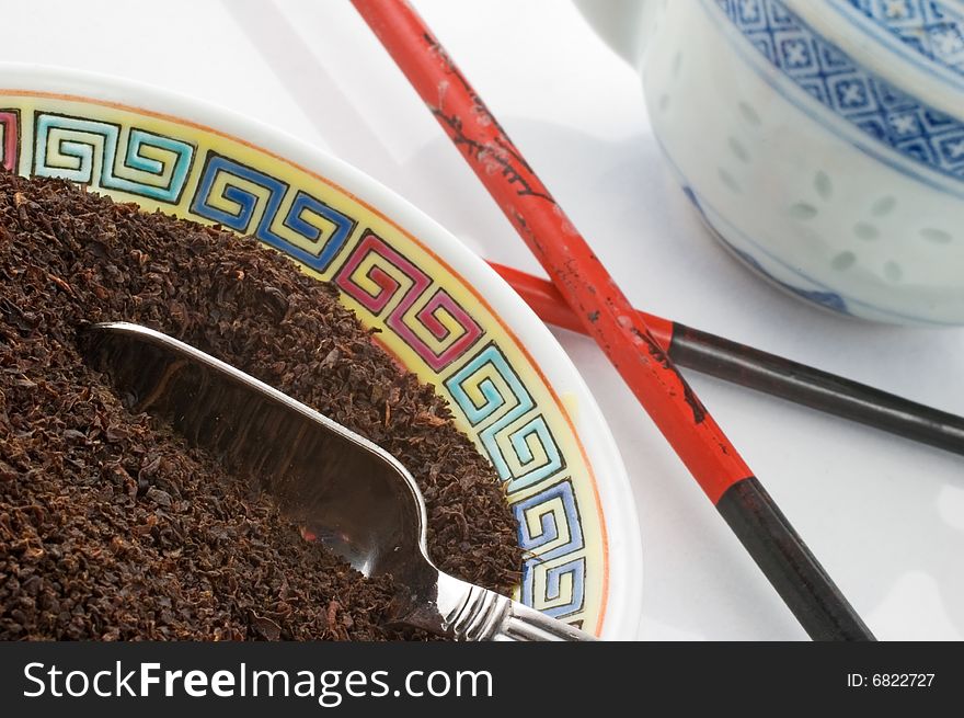 Tea leaves in bowl with chopsticks and teapot in the background. Tea leaves in bowl with chopsticks and teapot in the background