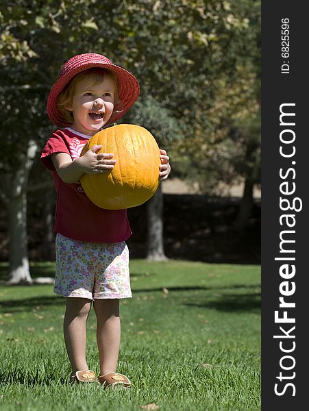 Child wearing a pink Hat Carrying a Pumpkin. Child wearing a pink Hat Carrying a Pumpkin