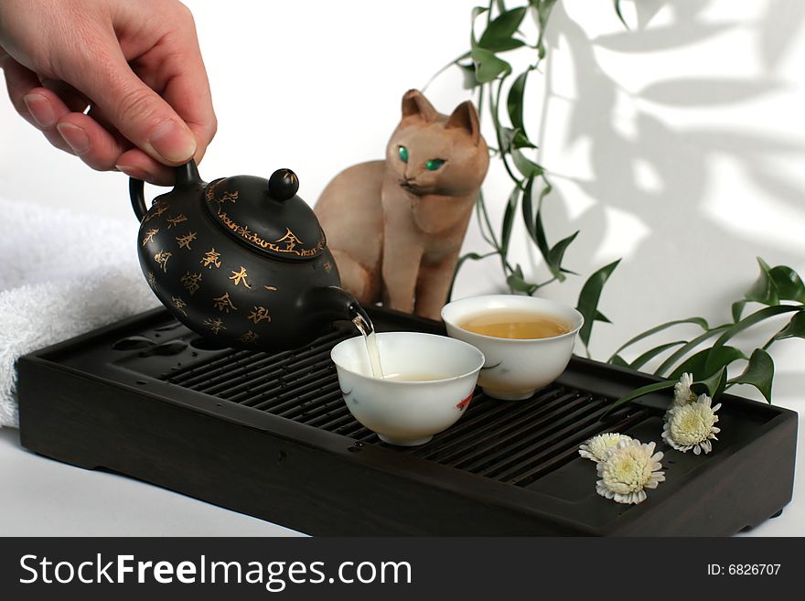 Green tea pouring into a white cup, on a wooden tray. Isolated on white background.