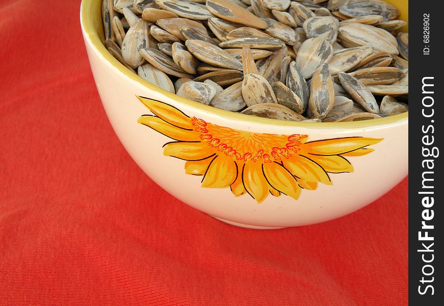 Sunflower seeds in a bowl with a sunflower decoration on red background