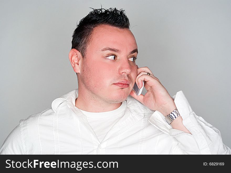 A young man having a conversation on a white cell phone.