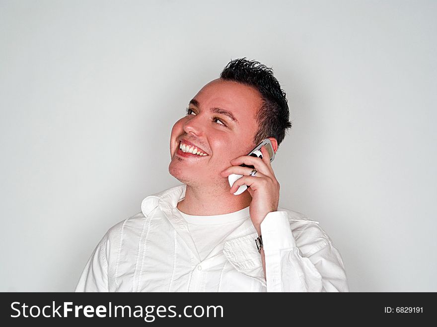 A young man having a conversation on a white cell phone.