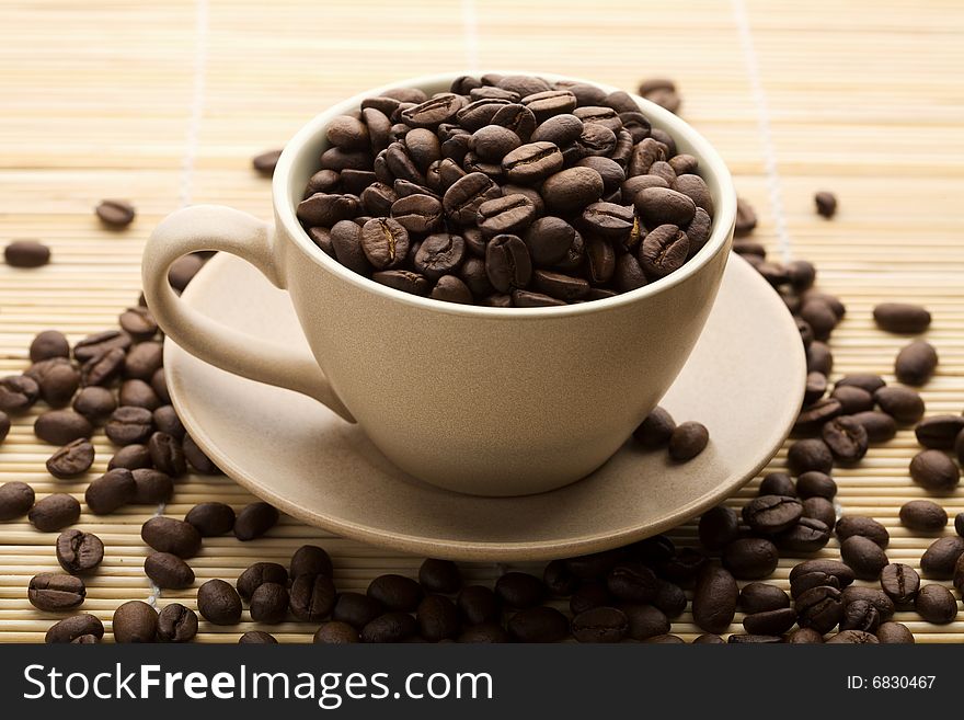 Cup of coffee beans over bamboo mat