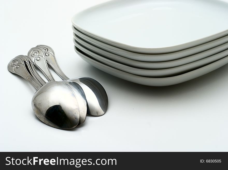 Pile of white plates and shining spoons on a white background. Preparation for table layout.