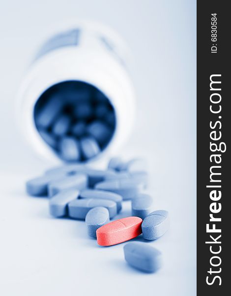 Blue prescription pills with one red pill over blue background