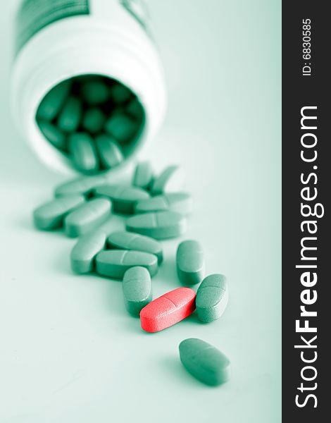 Green prescription pills with one red pill over green